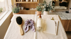 Flat lay of extension aftercare items on cream linen: a soft loop brush, silk scrunchie, sulfate-free bottle and a blank undated planner card