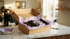 A brown kraft shipping box partly opened on a marble counter revealing tissue-wrapped hair extension bundles inside