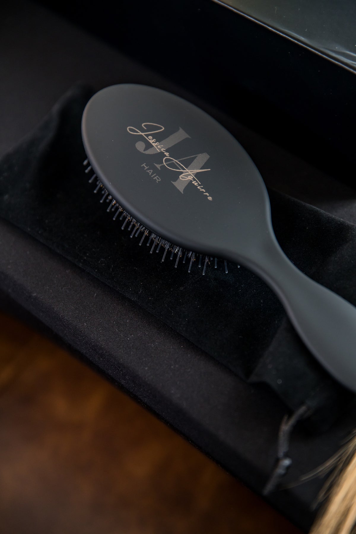 Matte black hair extension brush with personalized gold logo, in a velvet bag